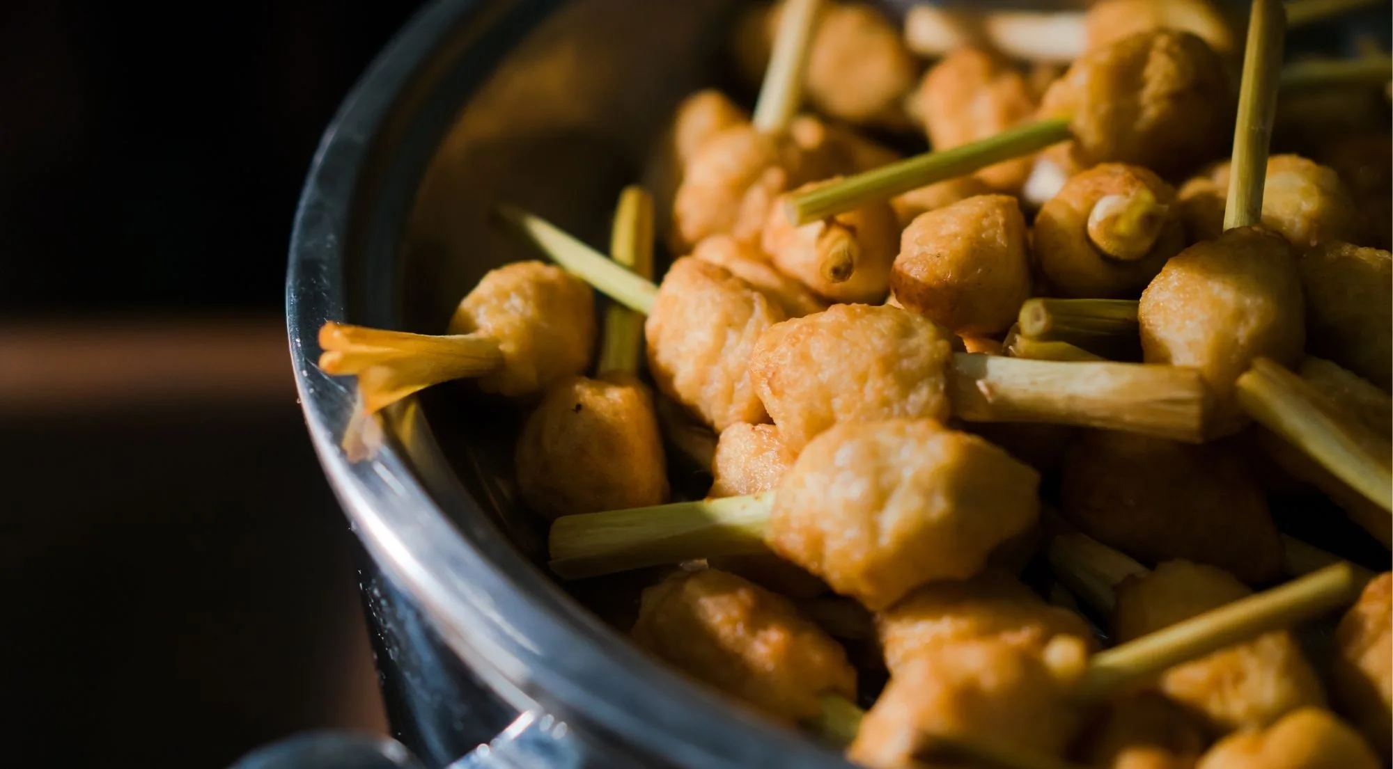 Bowl of hot battered pintxos on wooden skewers under bar lights