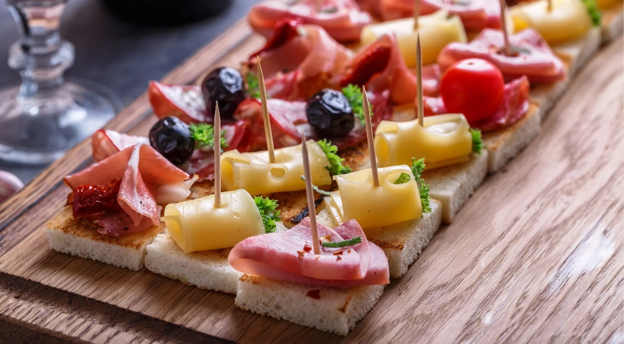 Board of pintxos with jamon, cheese and olives beside a wine glass