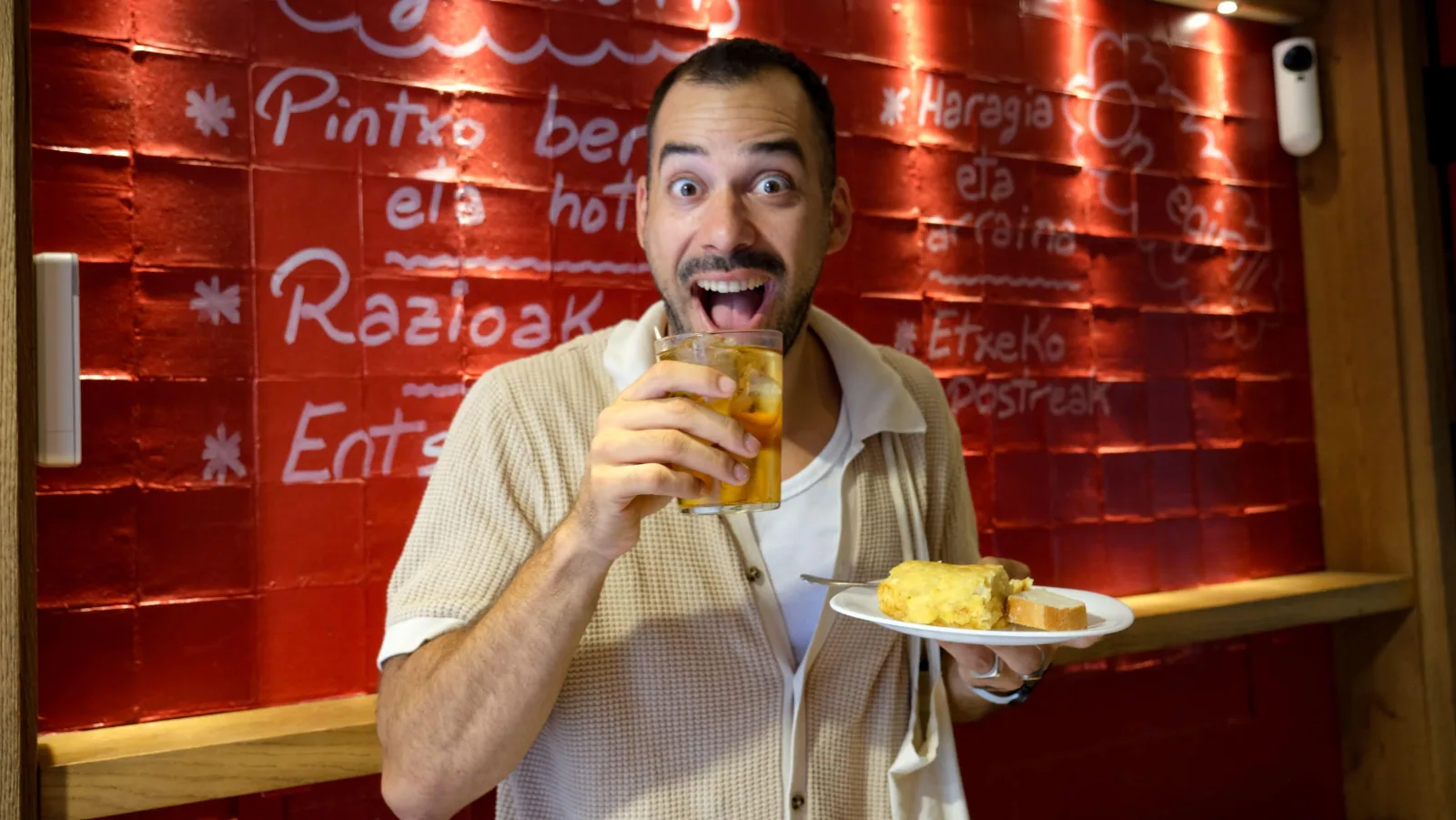 Guide holding a beer and a plate of tortilla in front of a red bar wall painted in Basque