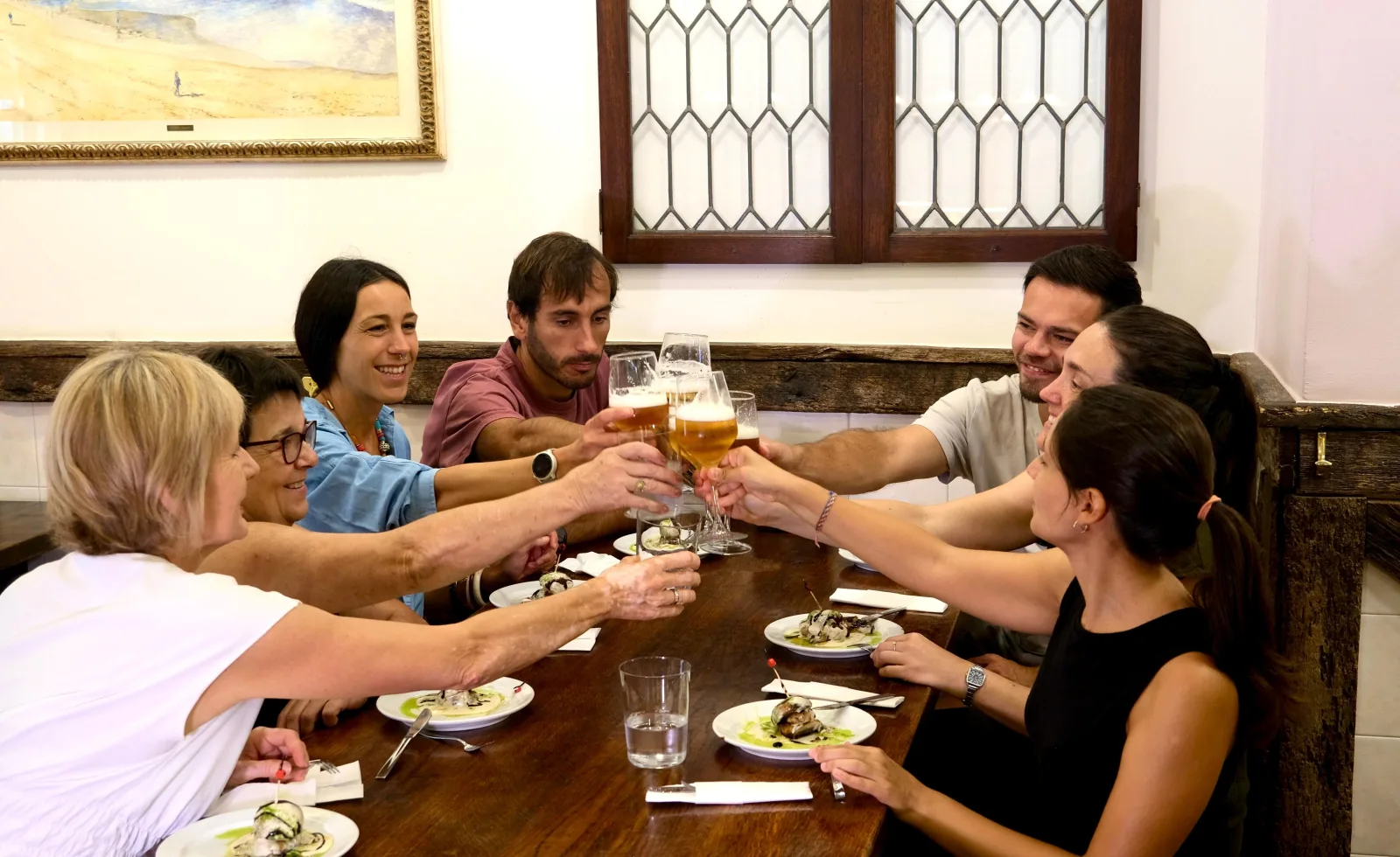Group toasting around a wooden table set with pintxos plates in a panelled dining room