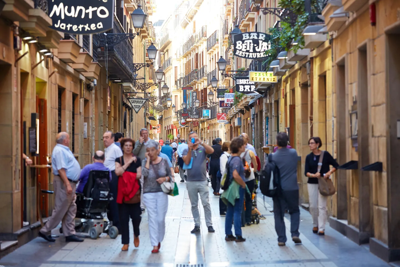 Visitors walking a narrow Old Town street lined with bar signs and restaurant awnings