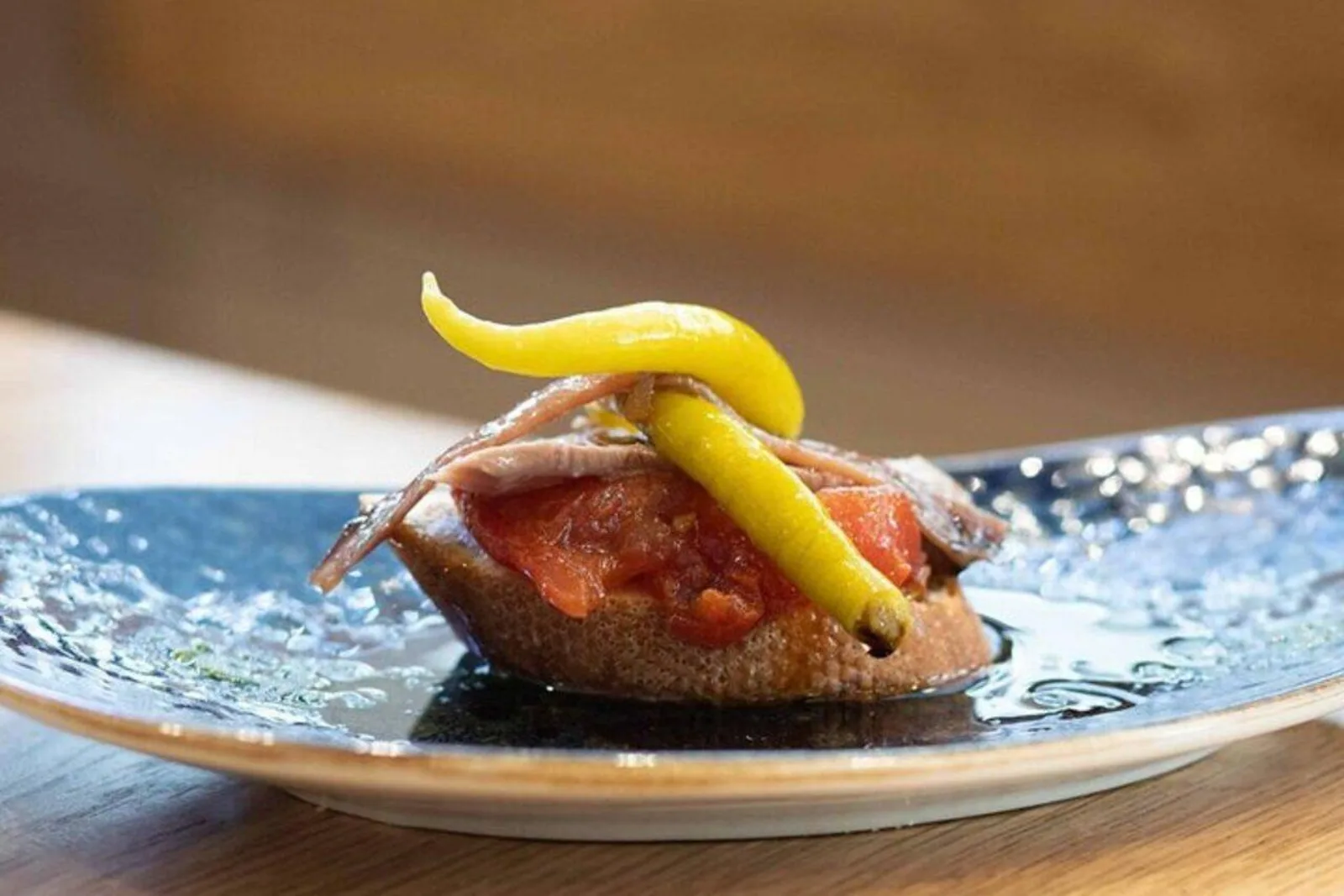 Pintxo of anchovy, guindilla pepper and tomato on toasted bread on a blue plate