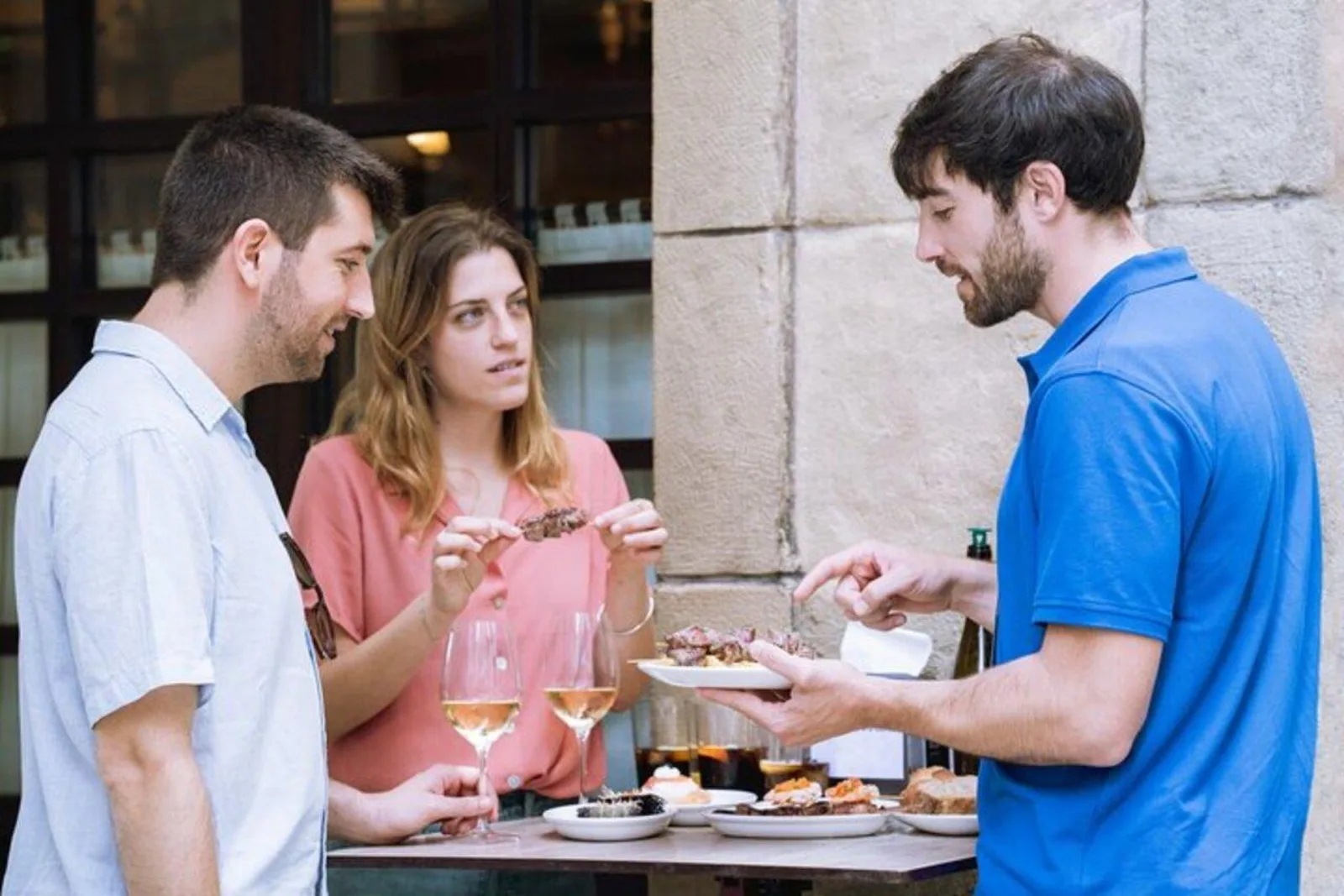 Guests holding wine glasses as the guide serves a plate of pintxos