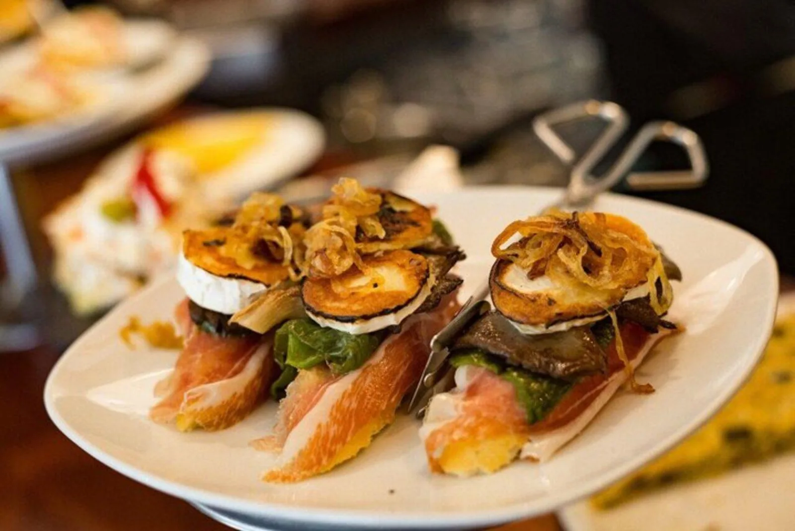 Stacked pintxos of jamon, aubergine and crisp onion on a plate at a bar