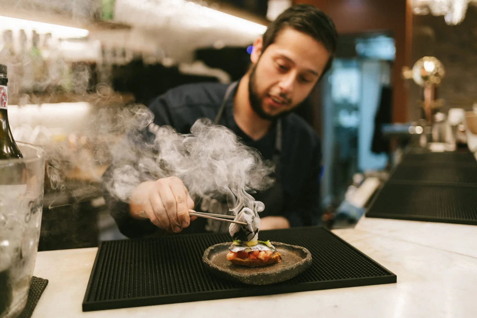 Bar cook searing a hot pintxo to order behind the counter, steam rising from the plate
