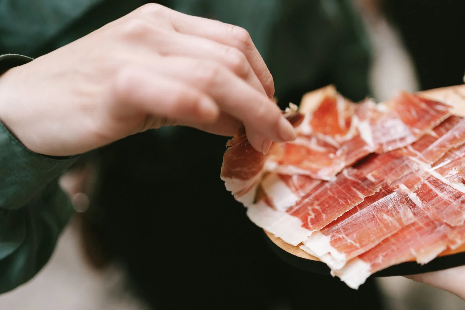 Hands lifting a slice of cured Iberian ham from a plate at a specialist ham shop