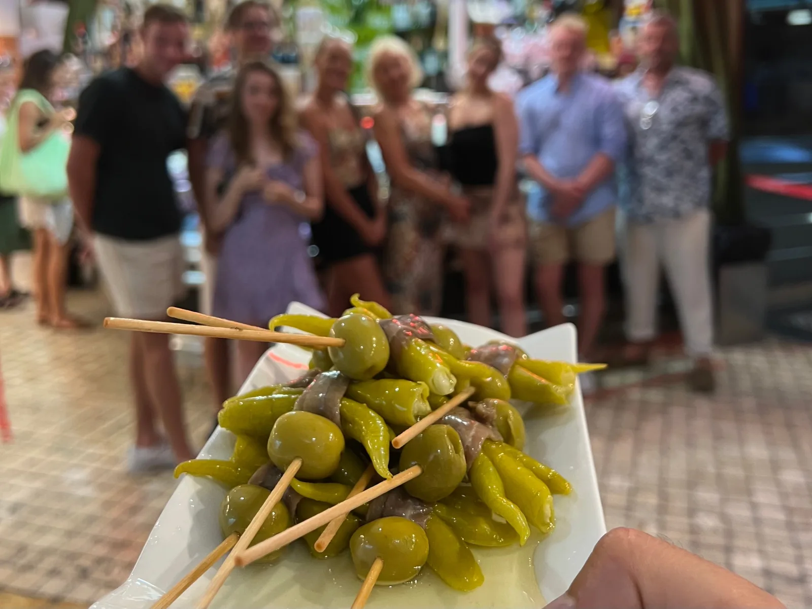 Plate of gilda skewers held up in front of the tour group in a busy Old Town street