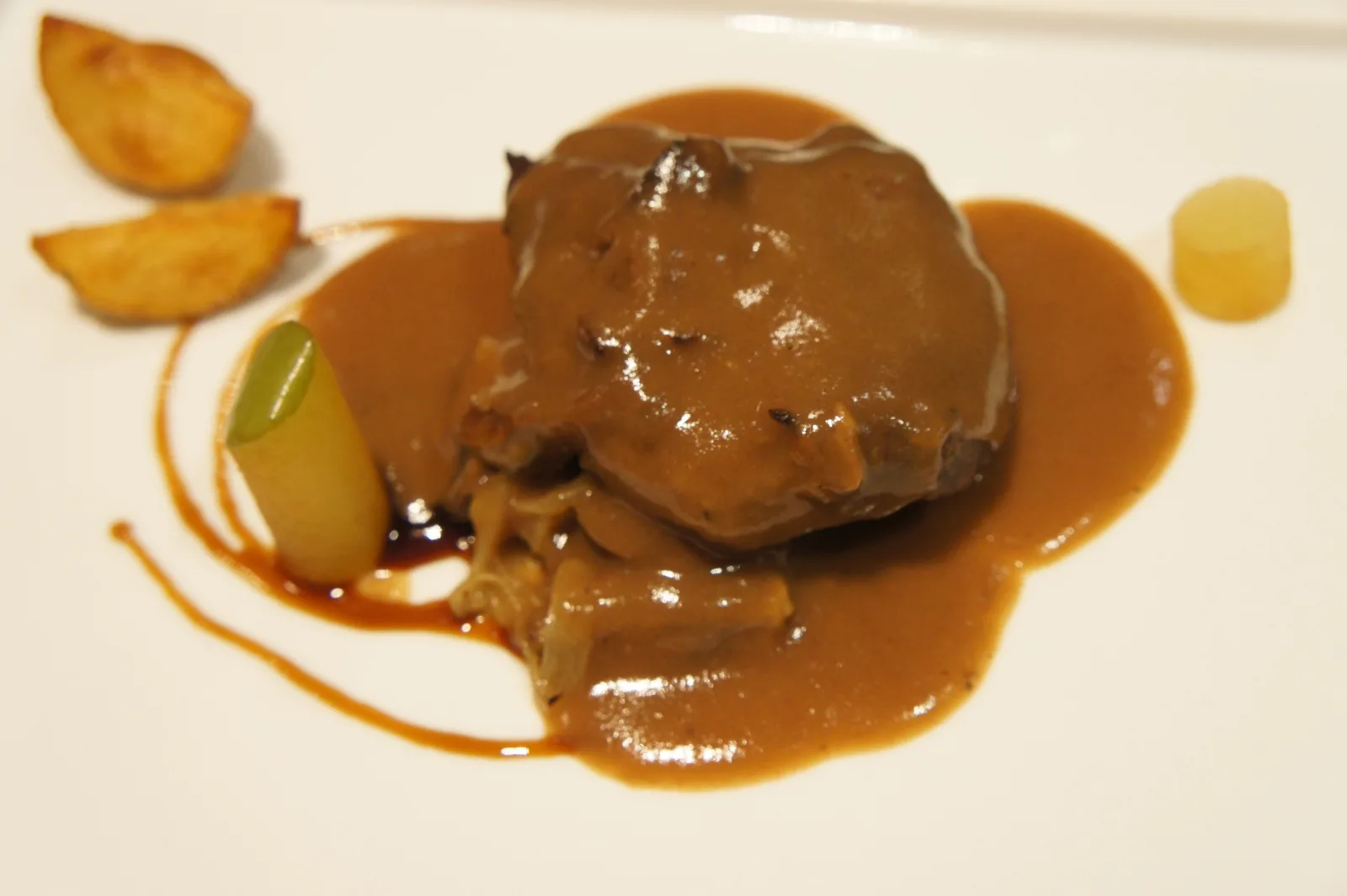 Braised beef cheek in red wine sauce with roast potatoes on a white plate