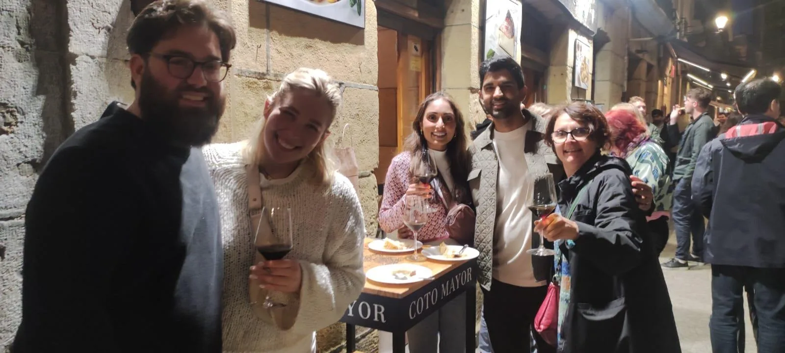 Guests holding wine glasses in a bar doorway on a busy evening in the Parte Vieja