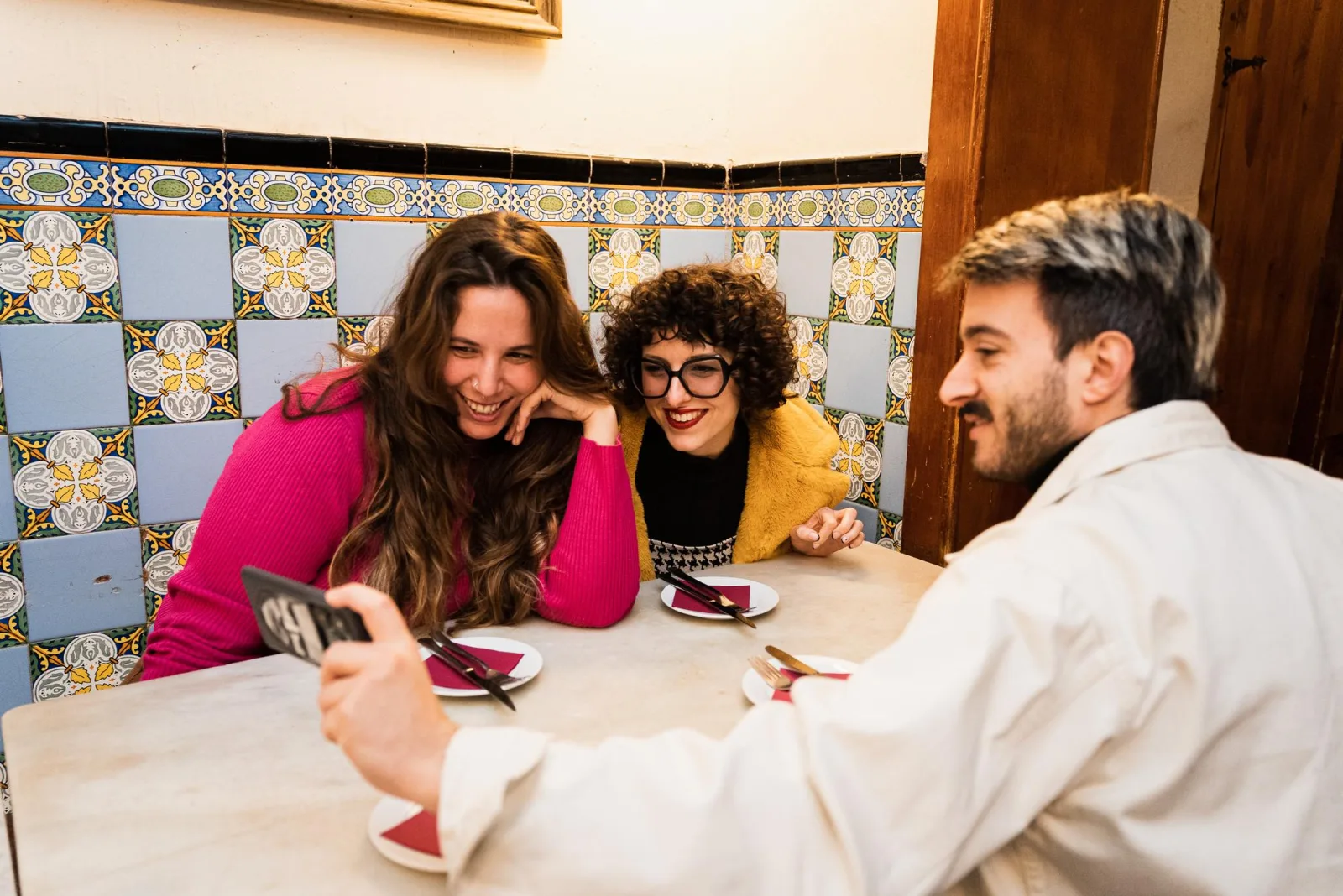 Three guests laughing around a tiled table with pintxos plates in front of them
