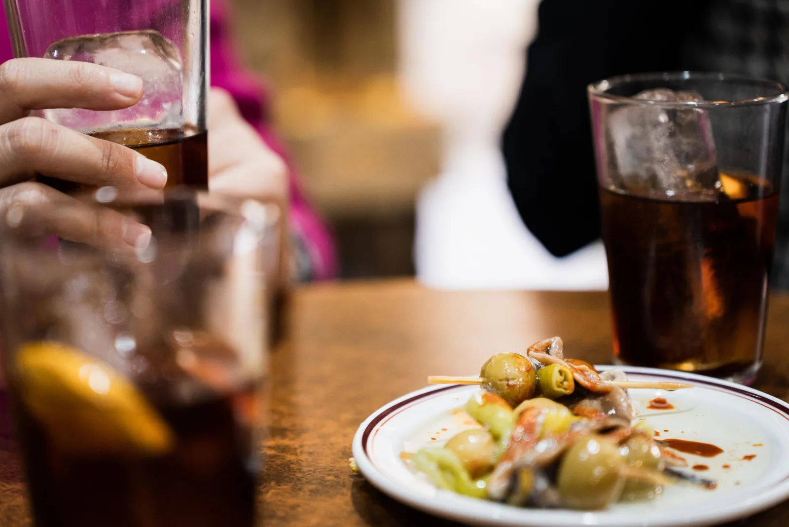 Vermouth on ice beside a plate of olive, anchovy and guindilla skewers