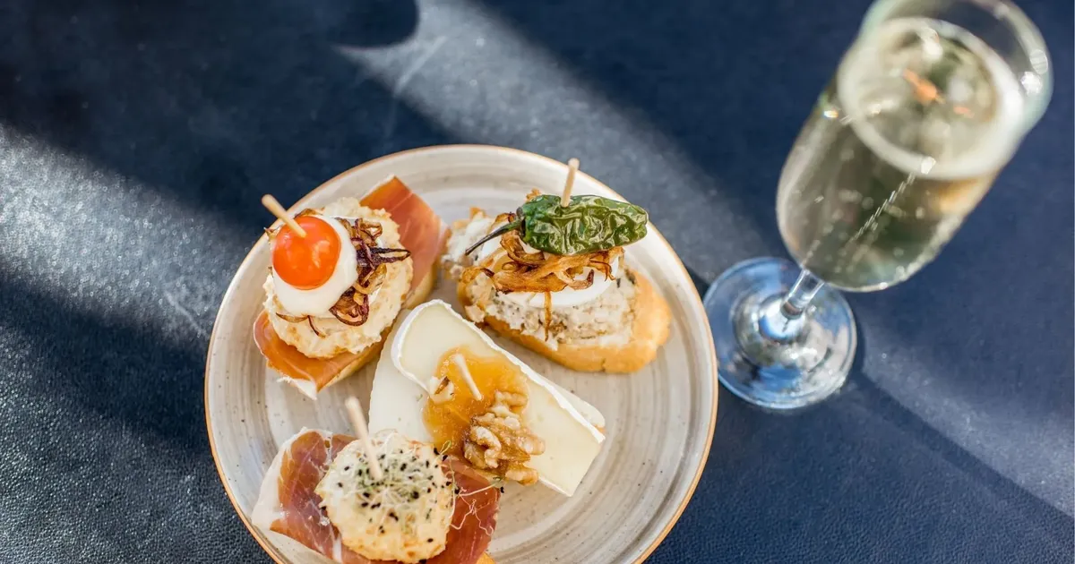 Pintxos on a plate beside a glass of sparkling wine