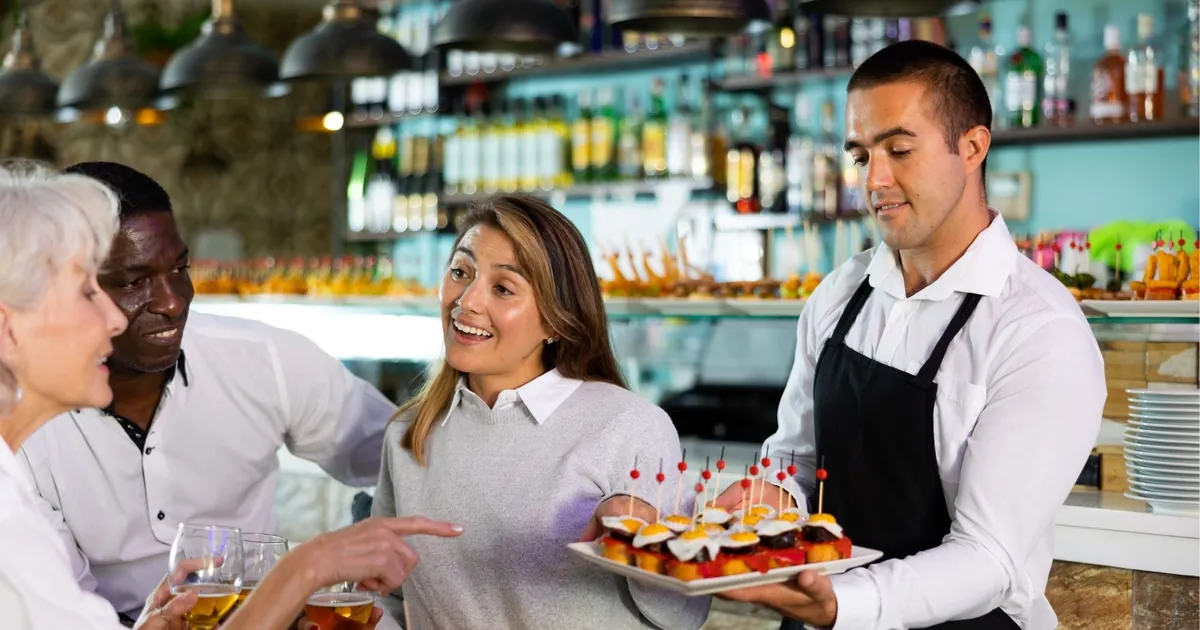 A bartender serving a tray of pintxos to guests at a San Sebastián bar